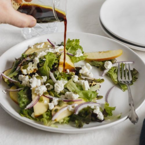 plate of salad with a hand drizzling a maple balsamic vinaigrette