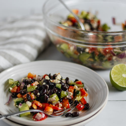a plate of black bean salad with a glass mixing bowl in the background